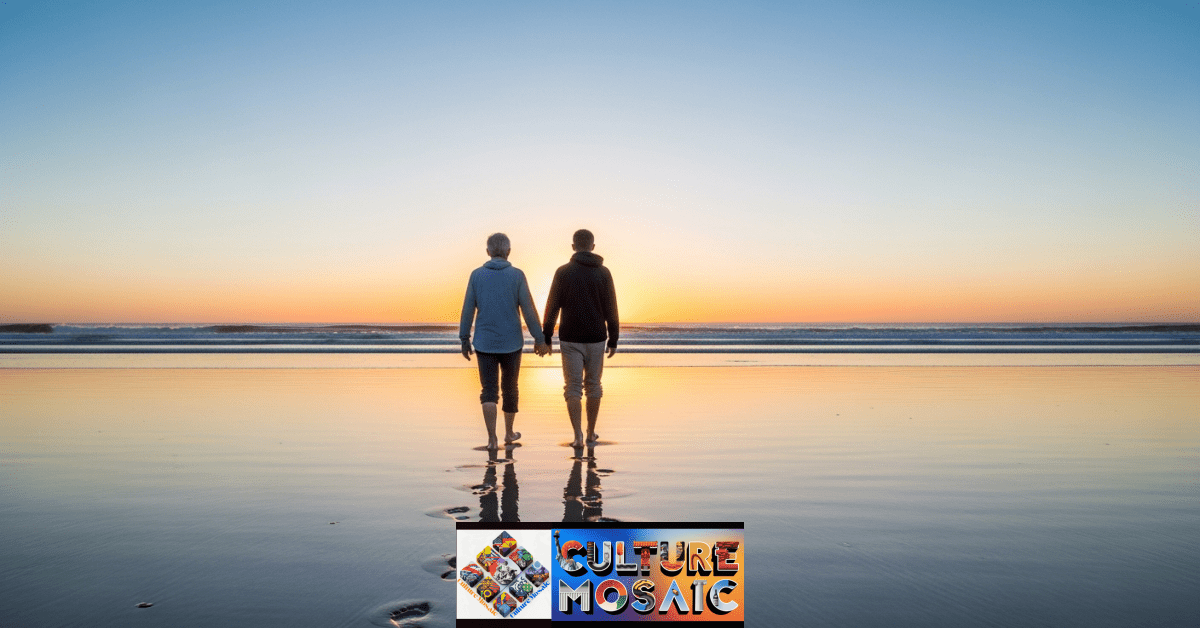 An elder and a younger person walking on a beach at sunrise, representing the journey of building new family stories.