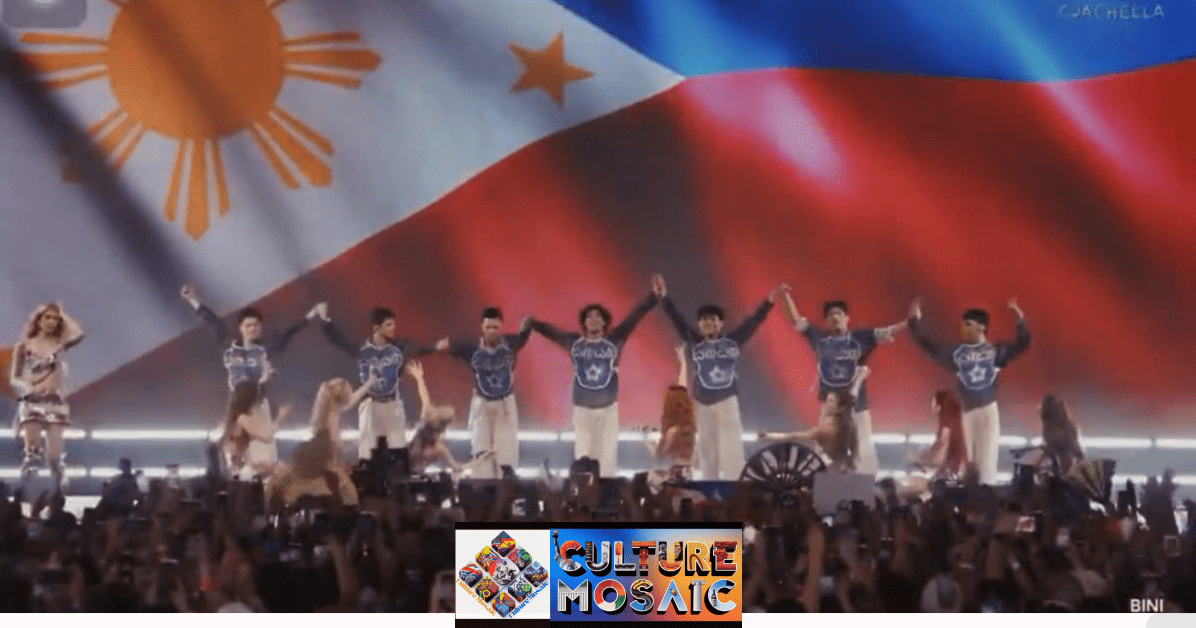 Wide-angle shot of BINI and their backup dancers standing in a line on the Coachella Mojave Stage, holding hands and raising them high in a final bow. A massive LED screen in the background displays a high-resolution, waving Philippine flag that fills the entire stage width. The foreground shows a dense, cheering crowd with numerous hands holding up smartphones to record the moment. Sheena Catacutan BINI is visible among the members in her metallic purple Weekend 2 performance outfit.