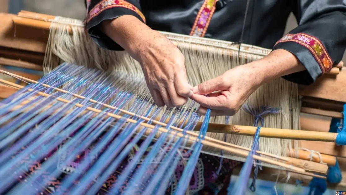 What is Heritage Fashion? An artisan hand-weaving intricate blue and purple threads on a traditional wooden loom, showcasing the craftsmanship behind heritage fashion.